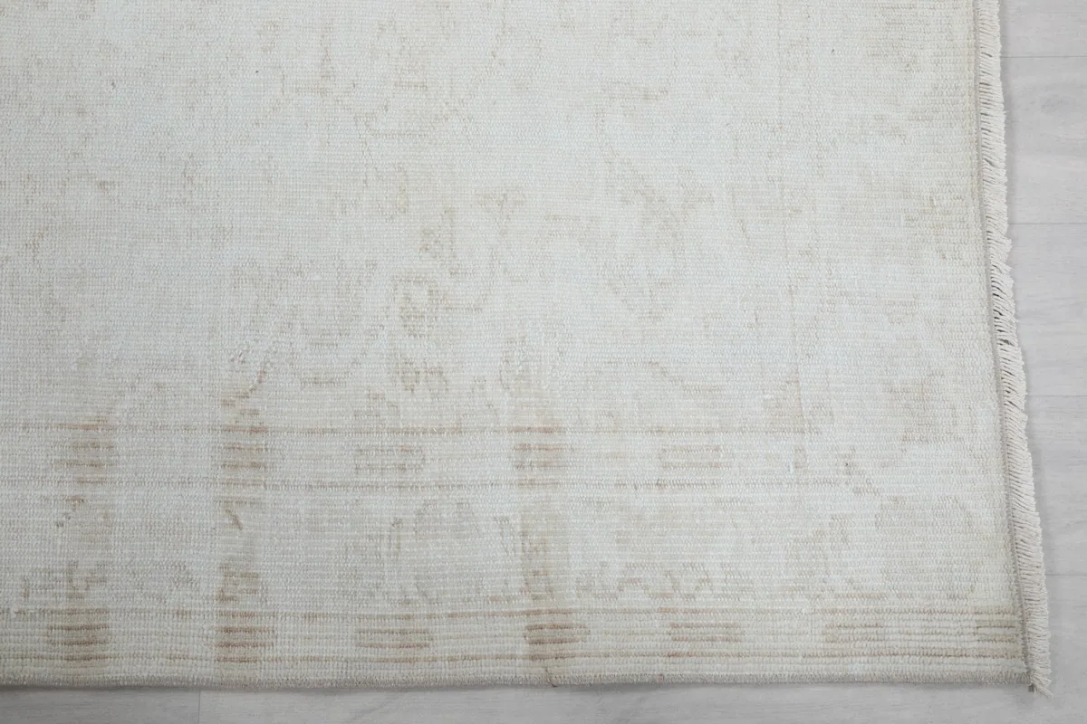 Detailed view of the rug's border and faded beige patterns on the ivory field