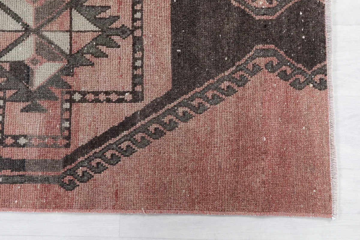 Detailed view of the rug's corner and border design, showing the faded rose and black tones.