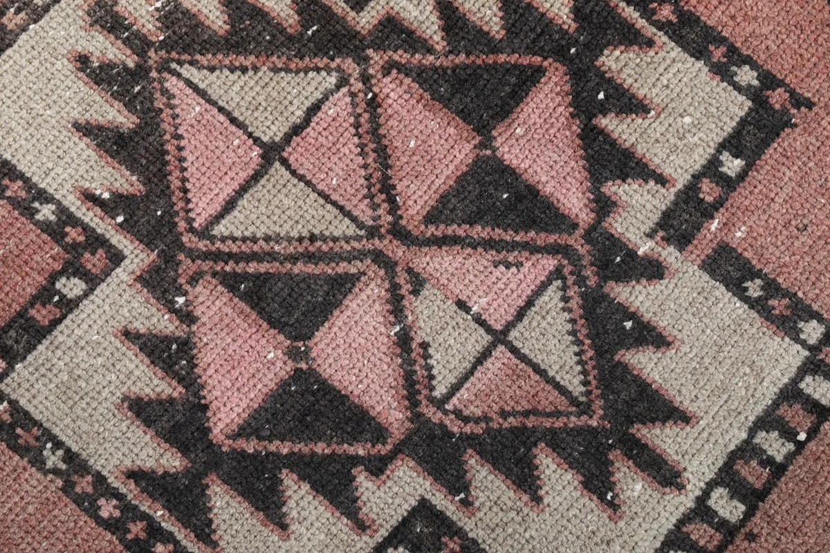 Macro detail of the hand-knotted wool pile and intricate geometric motifs in black, beige, and rose.