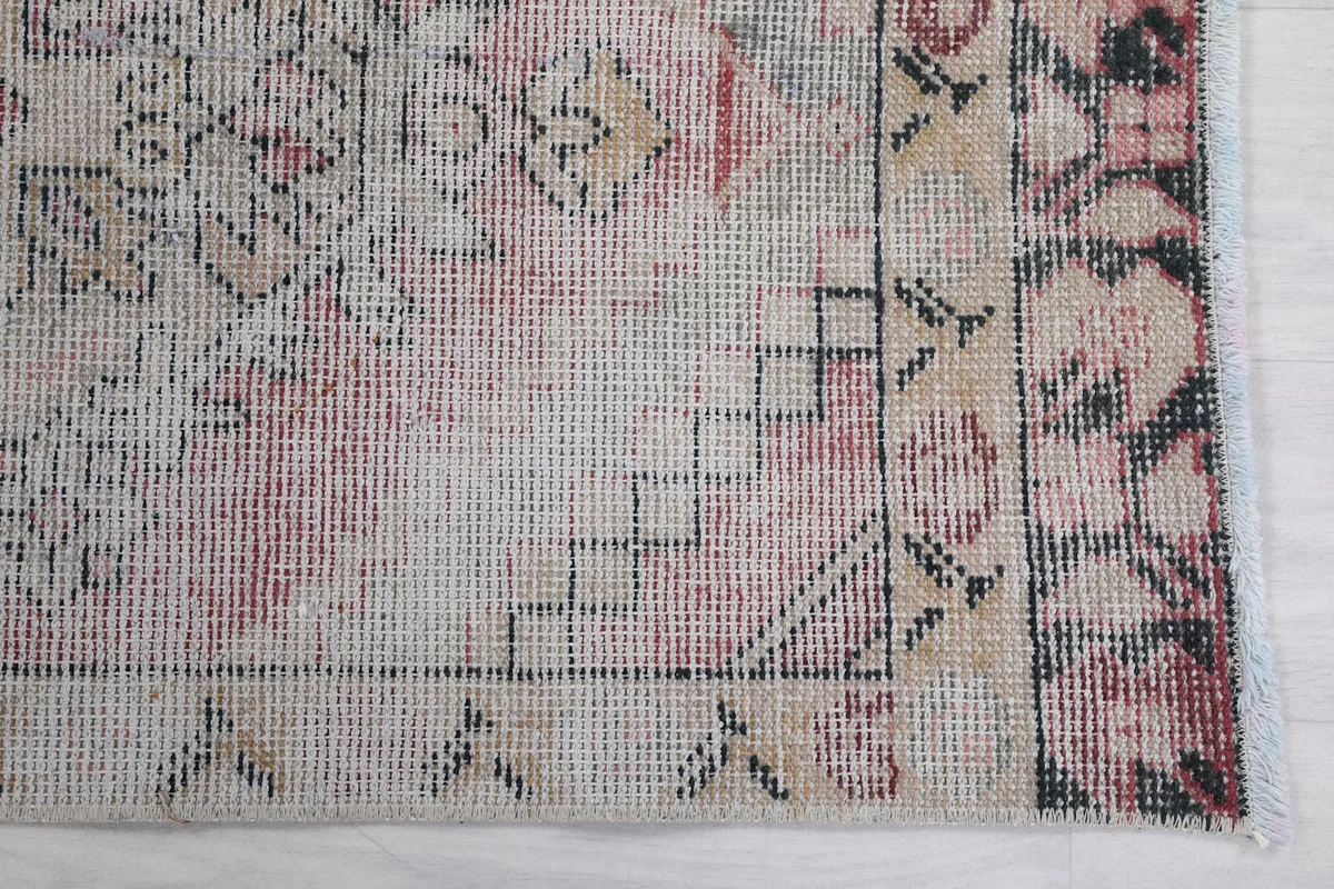 Detailed view of the rug's beige field and geometric border patterns in rose and black