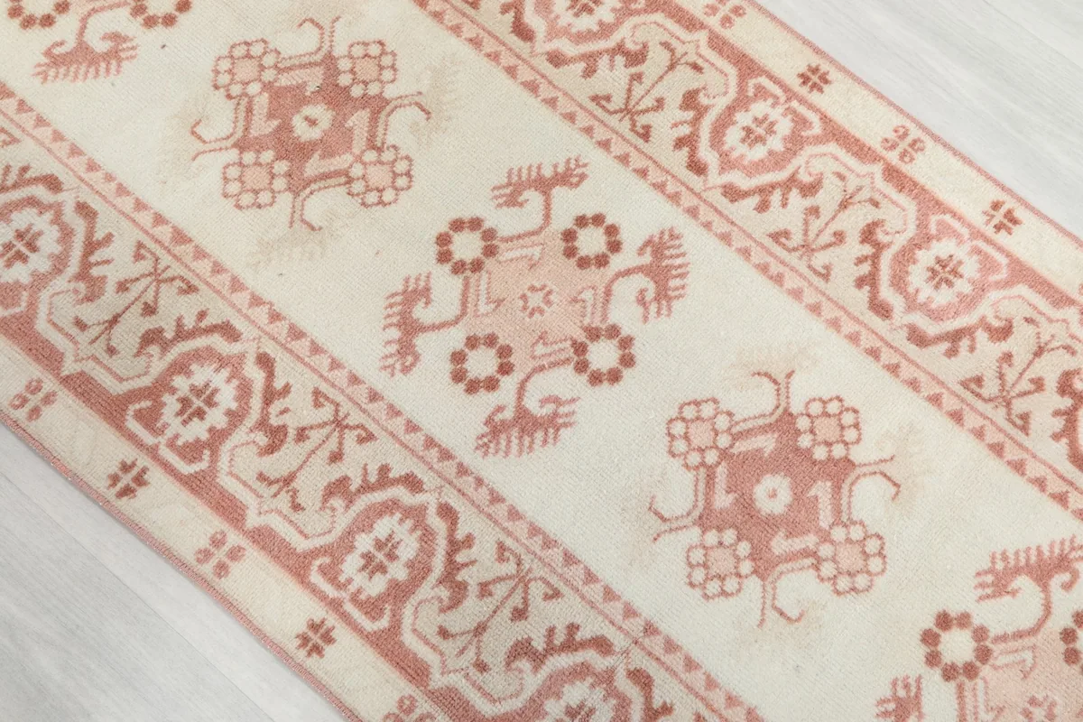 Angled close-up showing the repeated rose geometric motifs along the length of the ivory runner rug.
