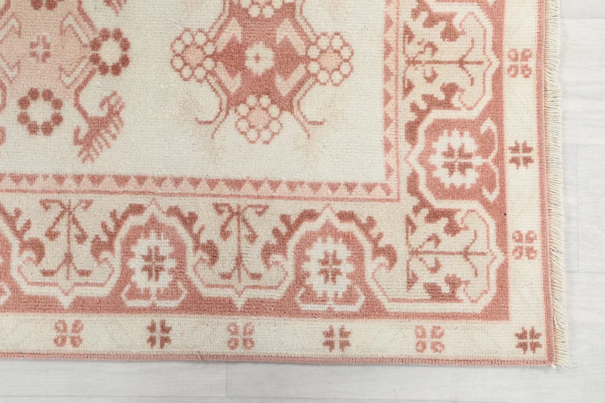 Detailed view of a corner of the rug, showing the rose geometric border and ivory field.