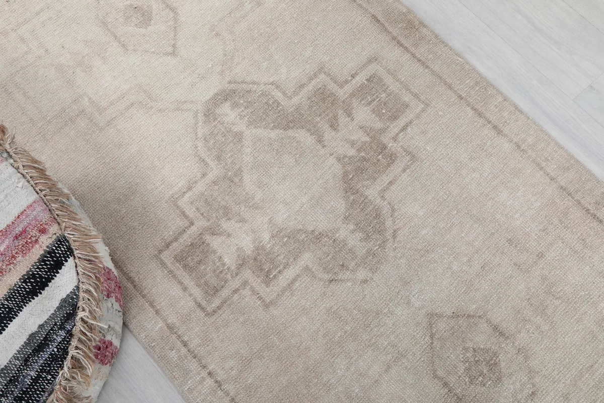 Detailed view of the central geometric motif in tan against the ivory field, next to a textured ottoman.