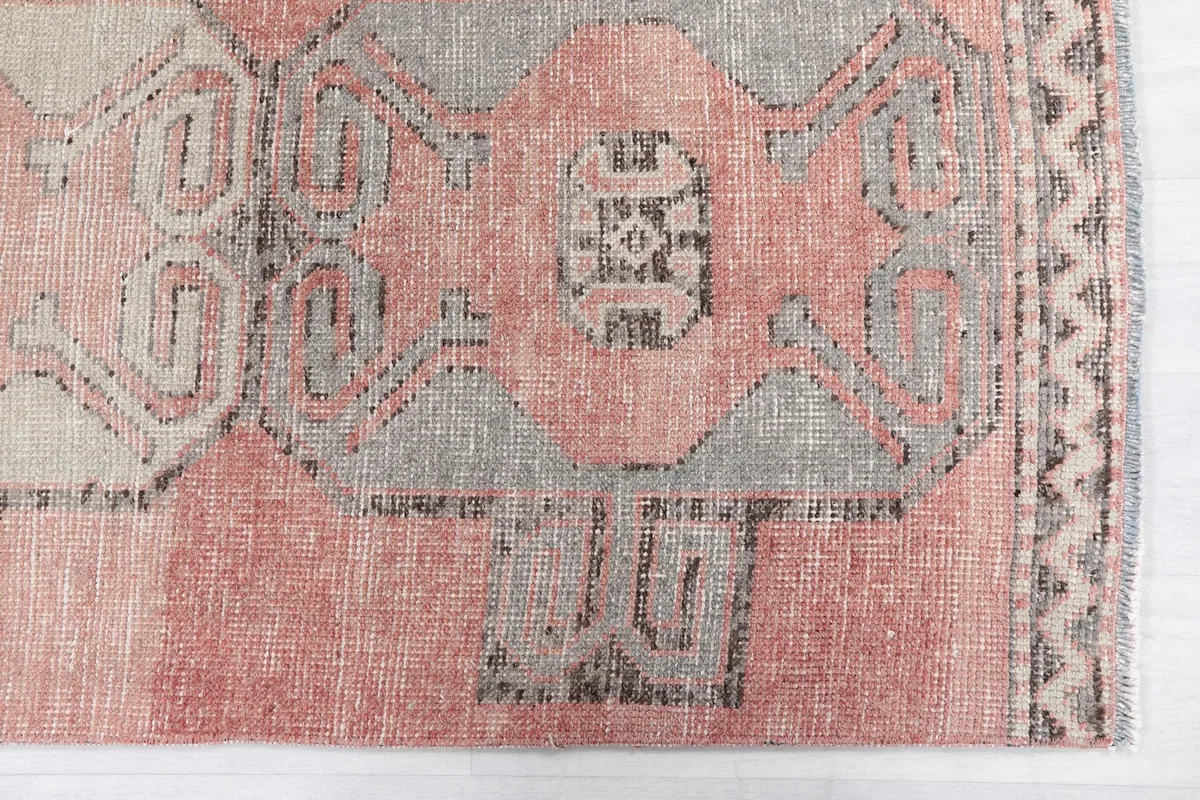 Detail view of the hand-knotted geometric motifs in gray and charcoal on the rose field