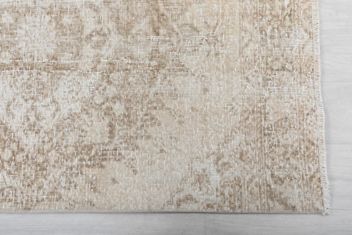 Detailed view of the rug's border and subtle geometric motifs in beige, ivory, and tan.