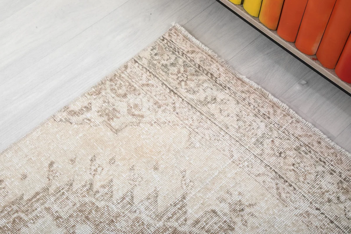 Close-up of the rug's edge, revealing the intricate, faded border pattern and natural patina.