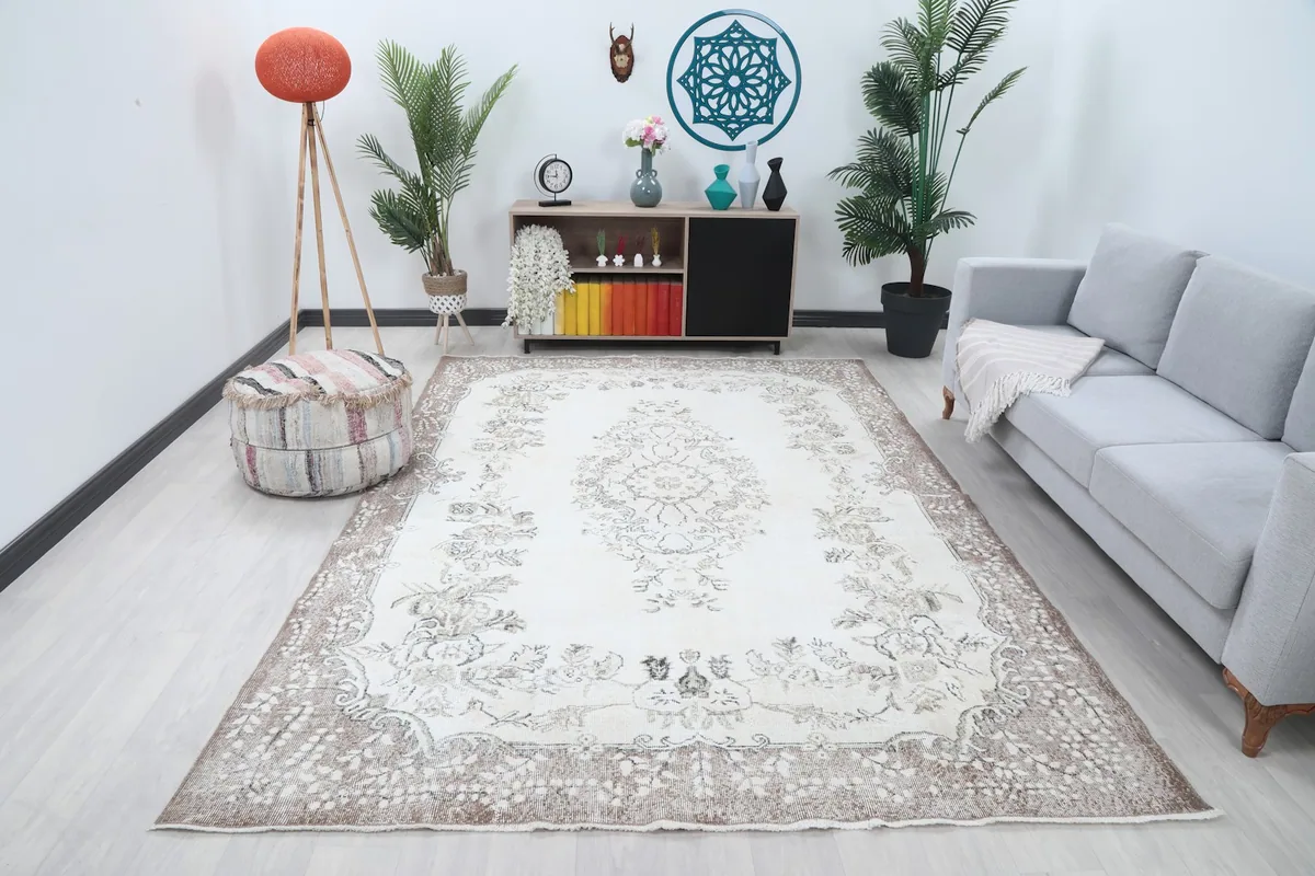 Vintage cream and beige rug laid out in a living room setting with a sofa and plants