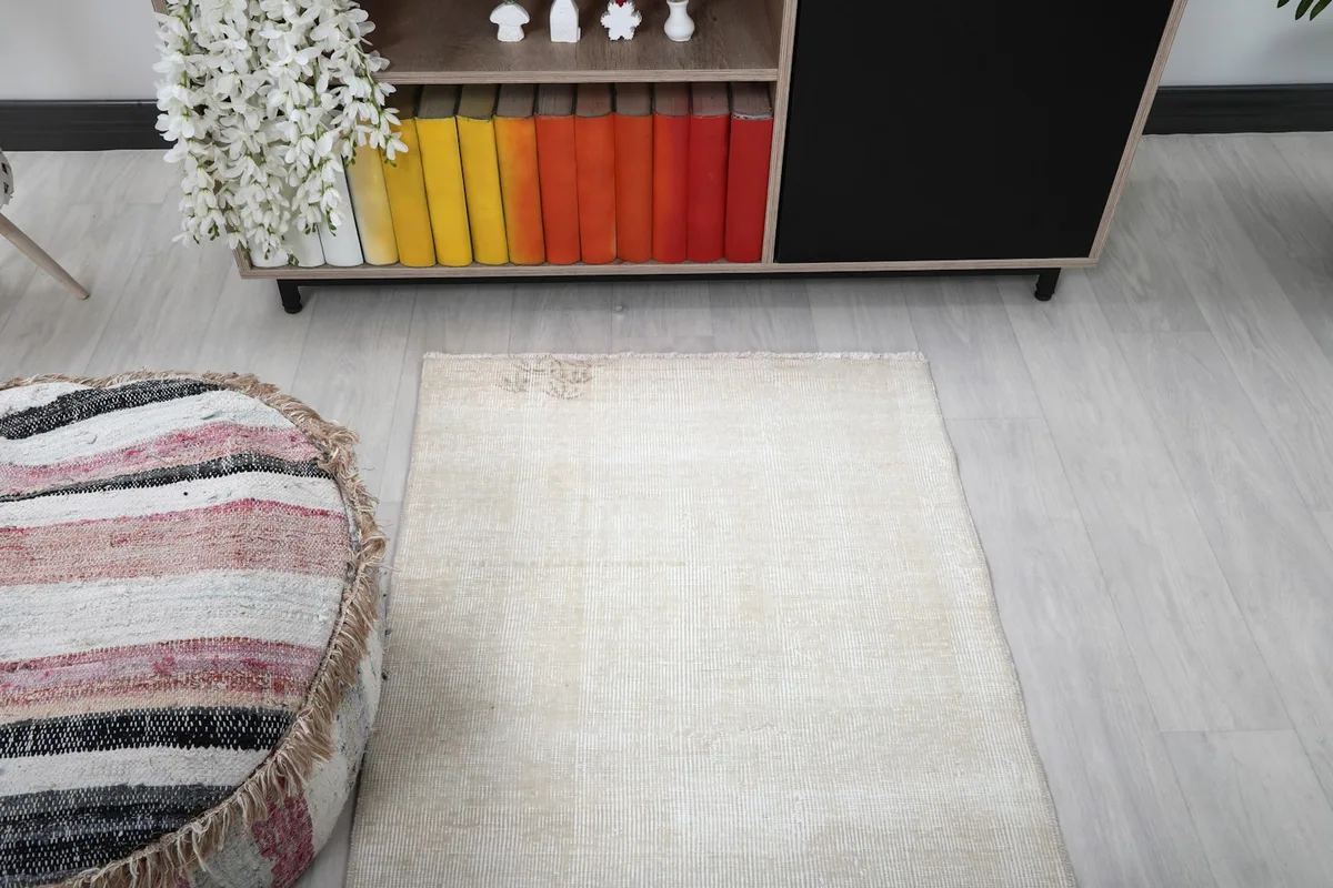 Corner view of the ivory rug in the room, showing its minimalist design and slight wear.