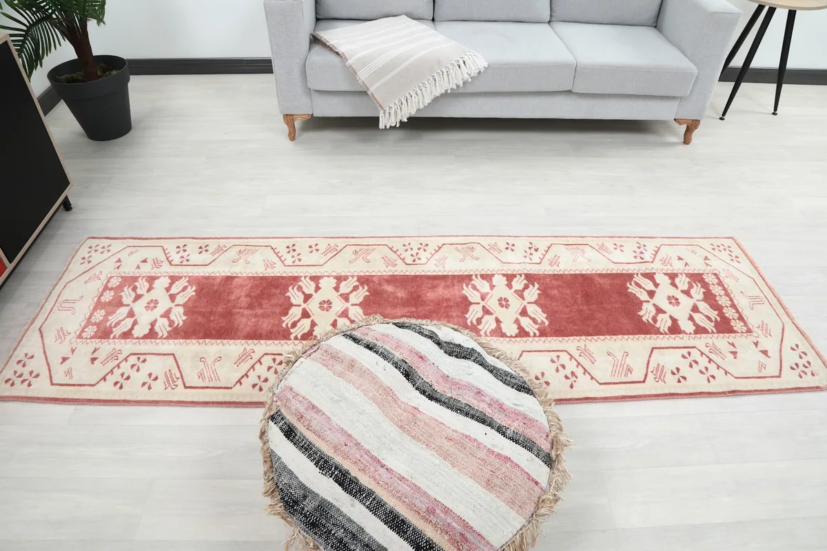 Overhead view of the rose and ivory runner rug in a room, with a pouf in the foreground