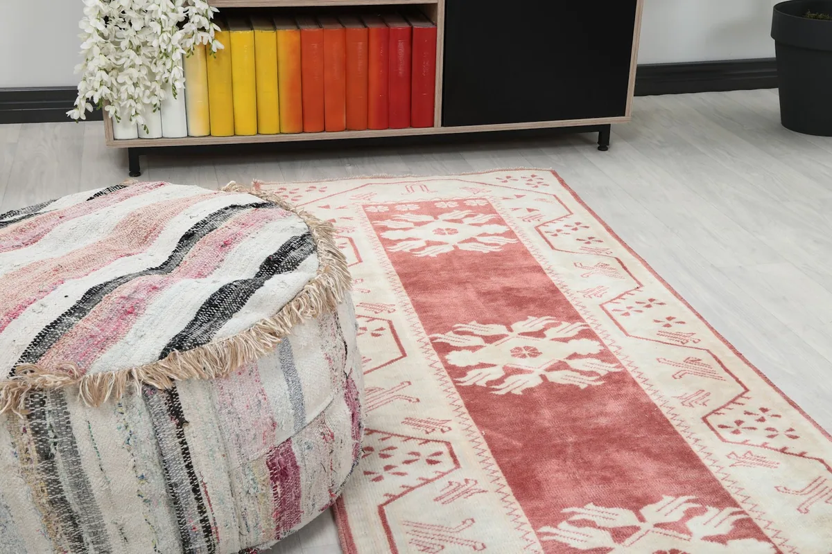 Close-up of the rose and ivory runner rug's pattern next to a striped pouf