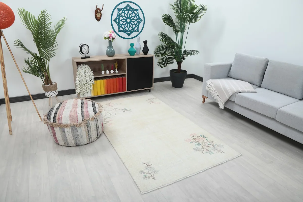 Angle view of the ivory area rug in a room, showing its placement relative to a striped pouf and sofa