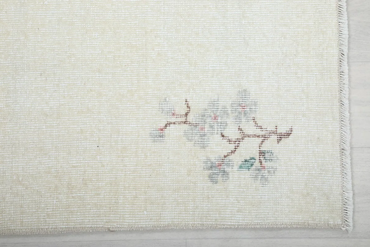 Detailed view of the rug's corner with faded green and brown floral patterns and fringe