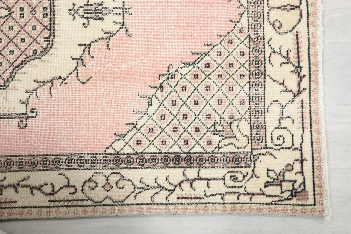 Detailed view of the corner motif and border pattern on the vintage pink and ivory rug