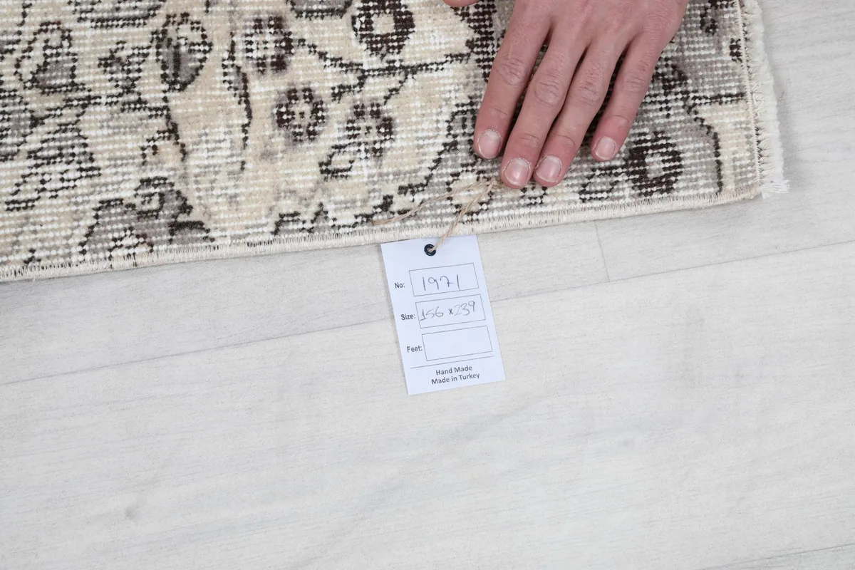 Hand holding a tag with rug dimensions 5'1" x 7'10" near the rug's edge