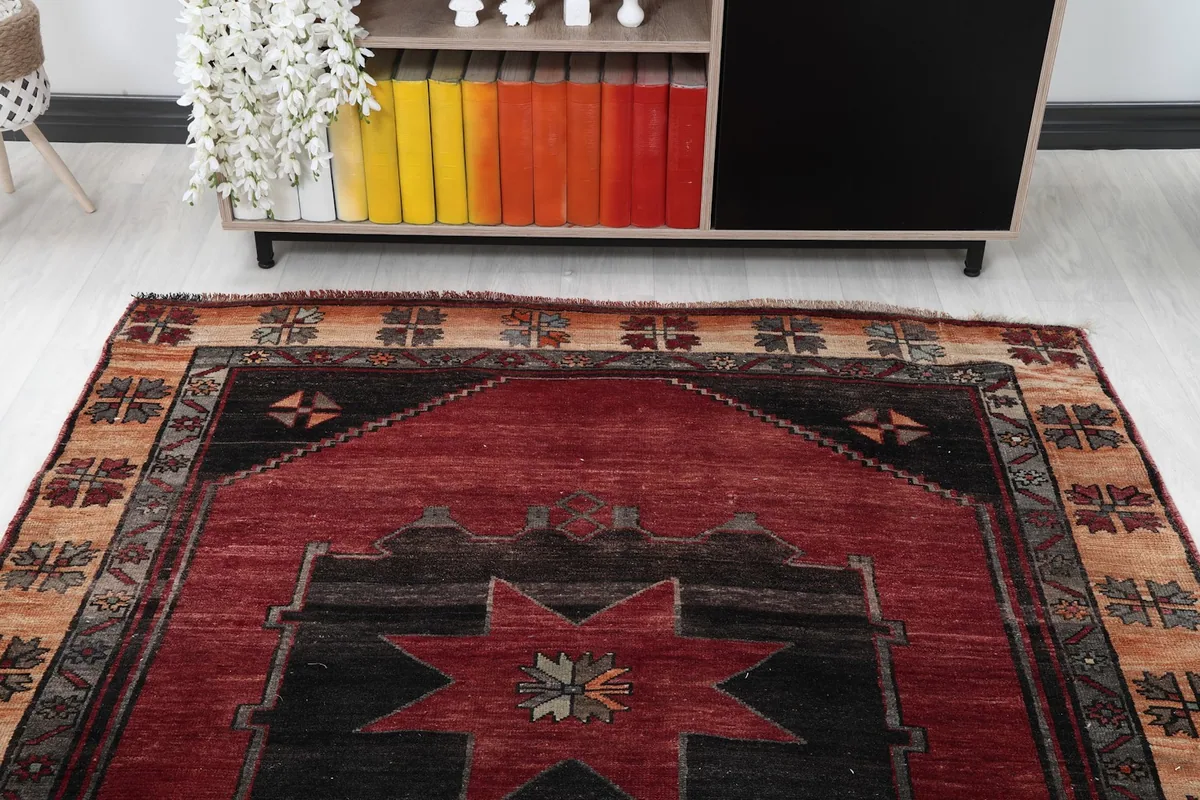 Top angle view of one end of the red vintage rug, showing the geometric pattern and border