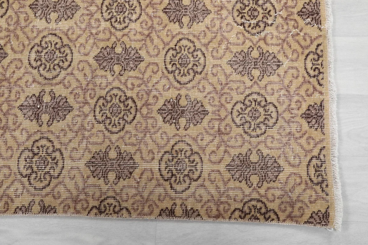 Detailed view of the repeating tan and gray floral and geometric motifs and rug edge