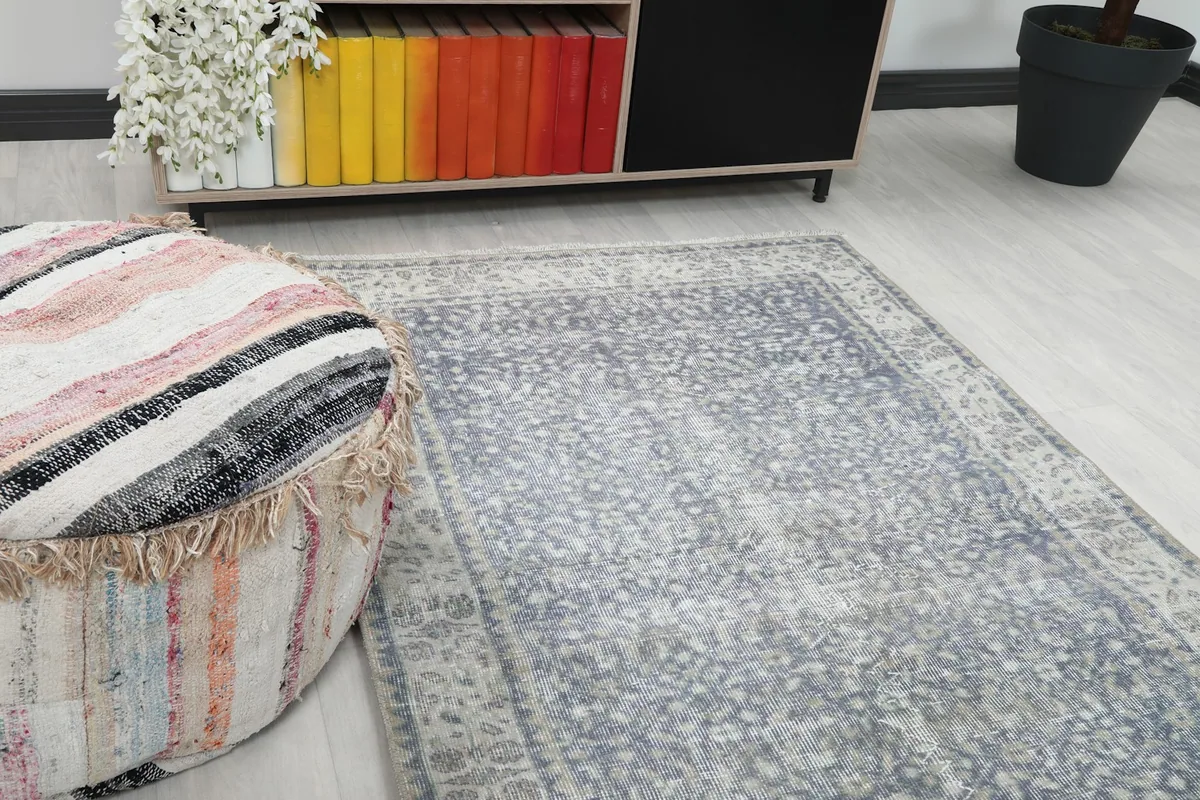 Close-up angled view of the gray rug's field and cream border next to a striped pouf