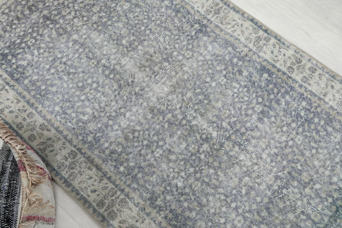 Angled view showcasing the faded gray and blue tones and intricate floral motifs of the rug