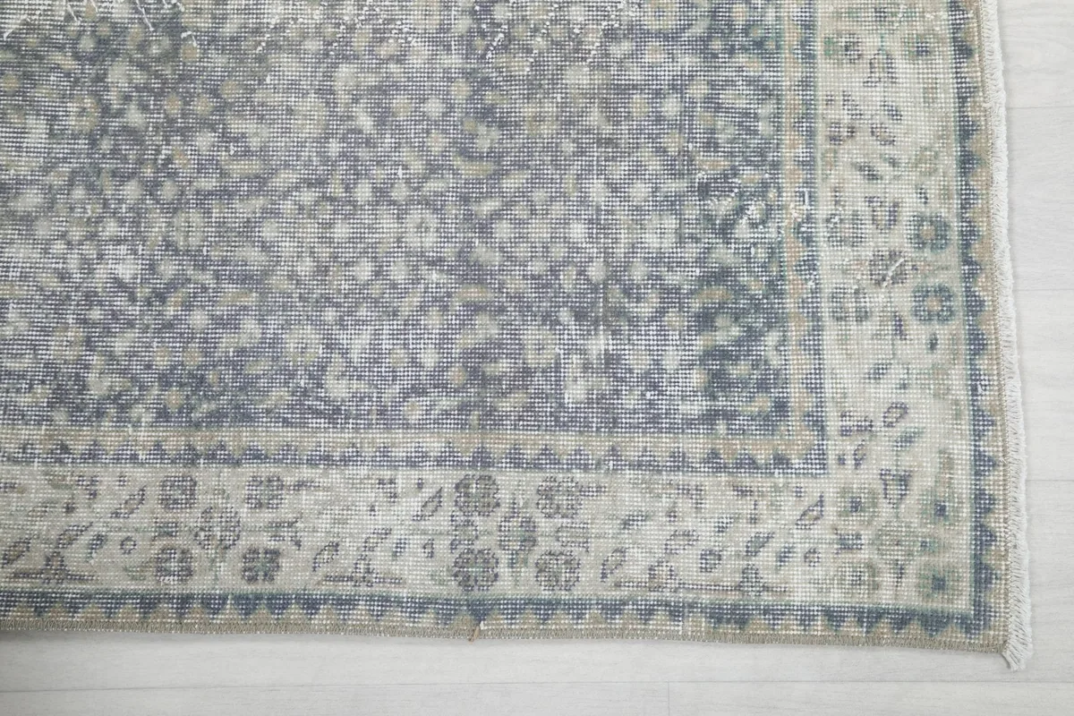 Detailed view of the cream border with blue and gray floral patterns and the faded gray rug field