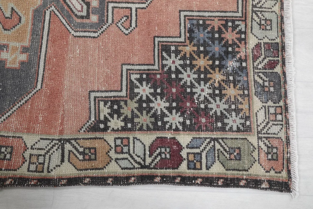 Detailed view of the corner of the rug, showing the geometric patterns and border motifs in rust, beige, and black