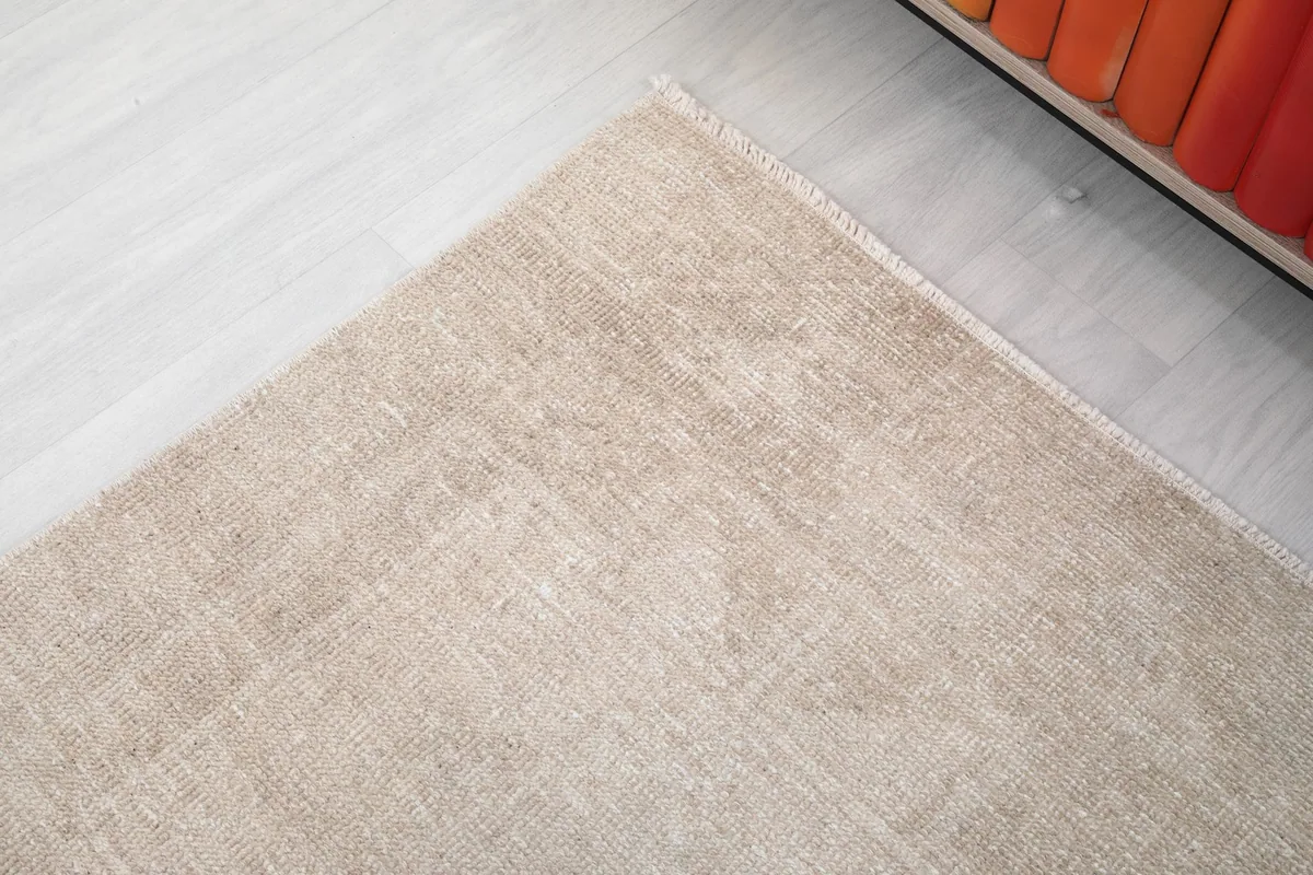 Detail of the rug's corner, showing the subtle edge finishing and the faded beige field.