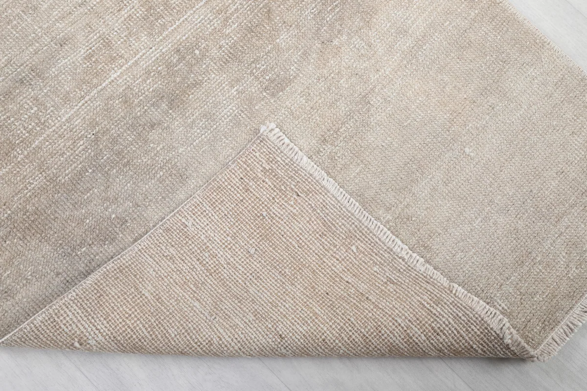 Corner of the rug folded back, revealing the cotton foundation and the reverse side of the hand-knotting.