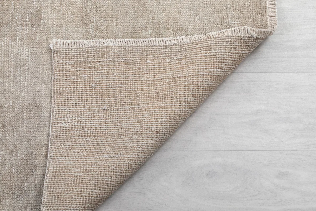 Another view of the rug's underside, showing the tightly woven cotton foundation and short fringes.