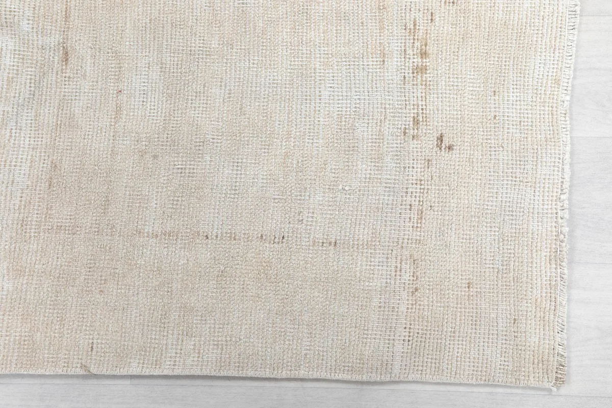 Detailed view of the rug's surface, highlighting the faded ivory and beige colors and wear