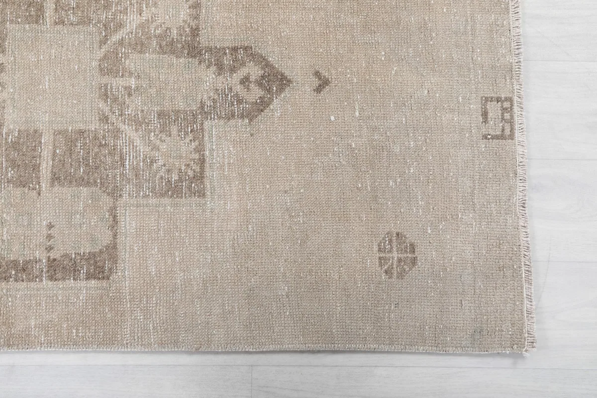 Detailed view of the beige rug's end, showing subtle gray tribal motifs and the fringe.