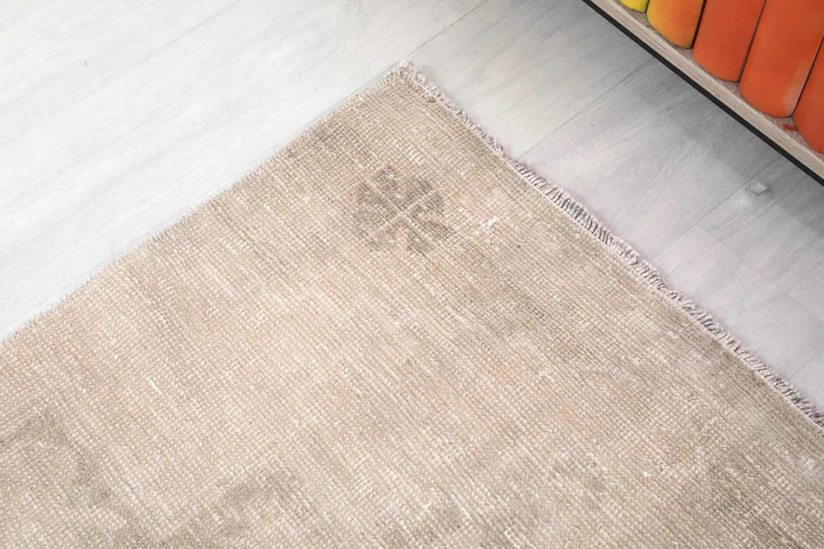 Detail of a corner of the beige runner rug, highlighting a small gray motif and the edge finish.