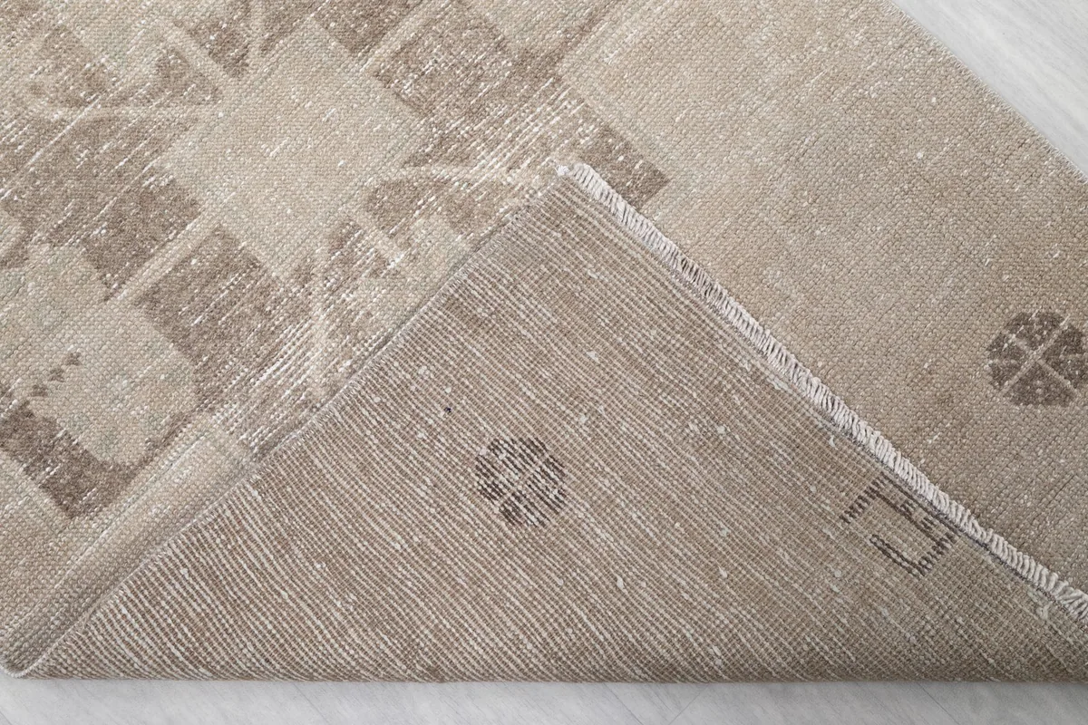 View of the back of the vintage beige runner rug, folded to show the hand-knotted cotton foundation.