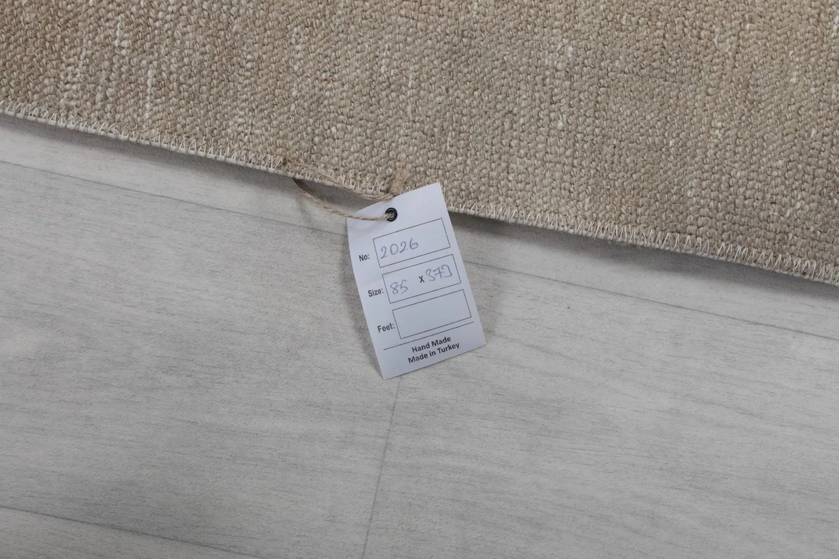 Close-up of the RugsKilim product tag attached to the vintage beige runner rug, showing its details.