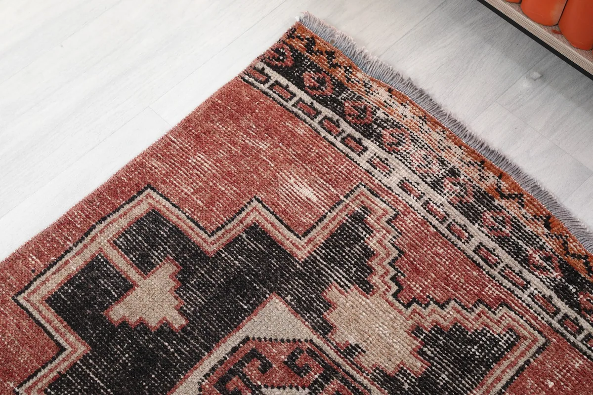 Corner detail of the runner rug, showing the border design and faded black and rust tones.