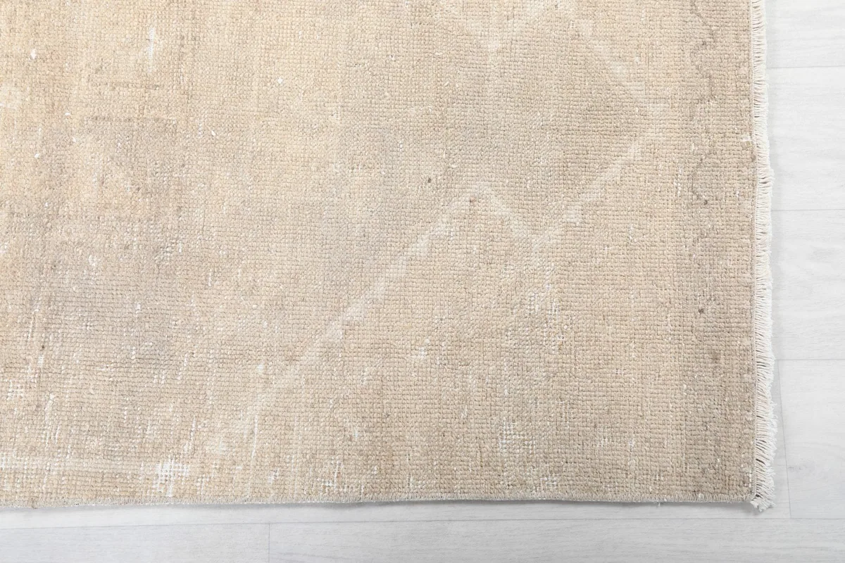 Close-up of the rug's edge, showing the low pile and subtle beige geometric pattern on the tan background