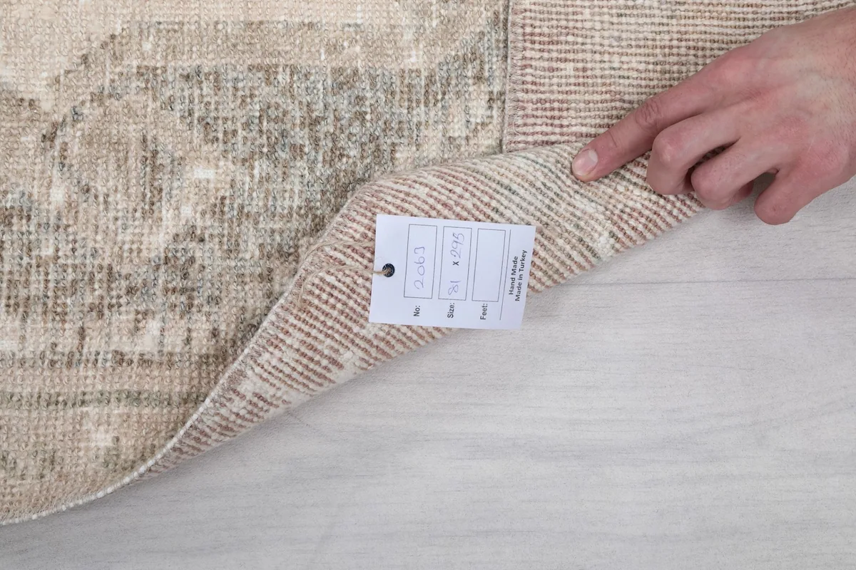 Hand lifting the rug to show the label and the texture of the back