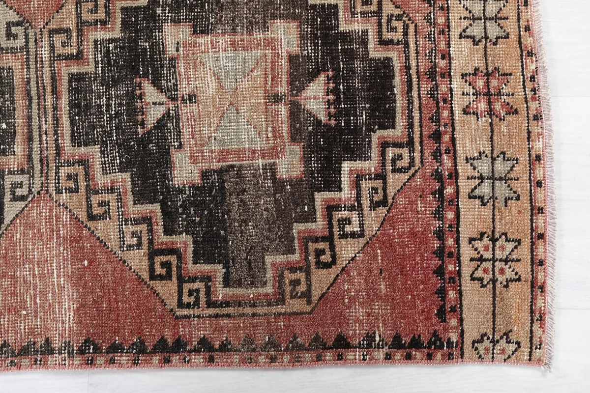 Detailed view of the geometric medallion and border design with faded rust and black tones