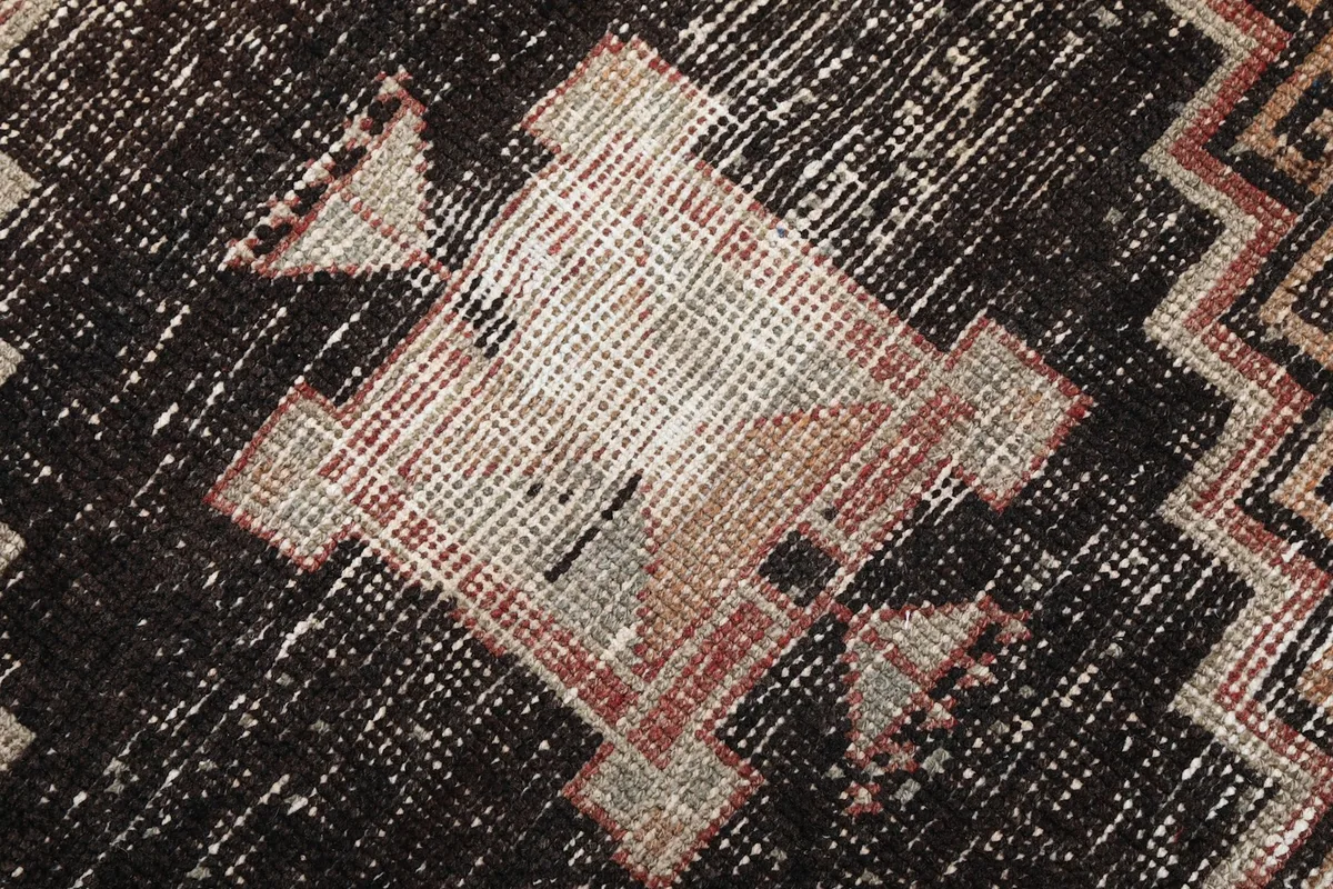 Close-up of the low wool pile and intricate black, rust, and beige geometric weaving