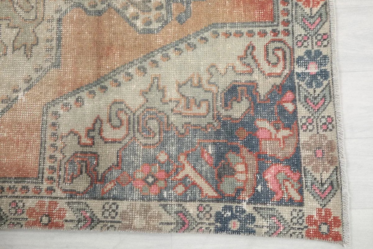 Detailed view of the rug's corner with blue, pink, and rust tones in the border and field