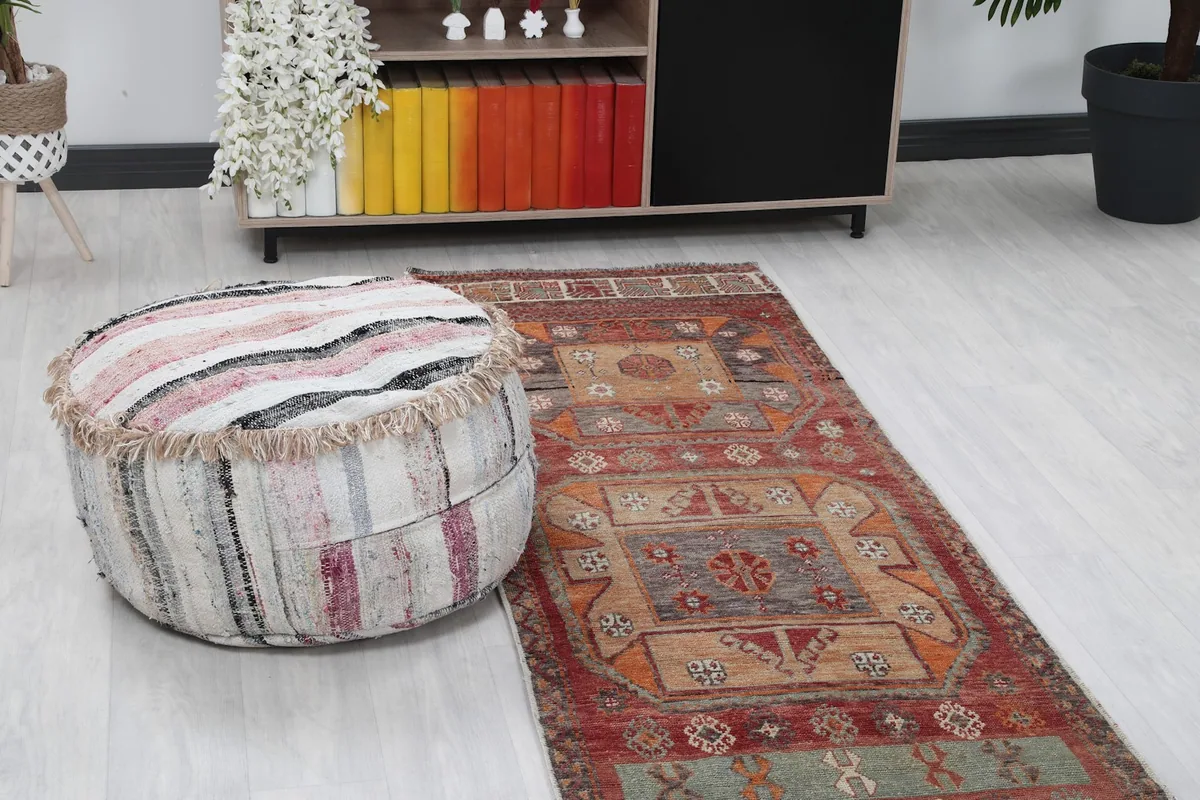 Close-up of the vintage runner rug's pattern and colors, with a decorative pouf in the foreground