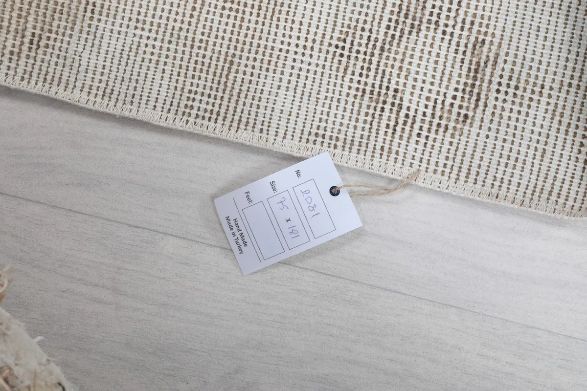 A tag with rug information, lying on the floor next to the rug's edge, showing details like size.