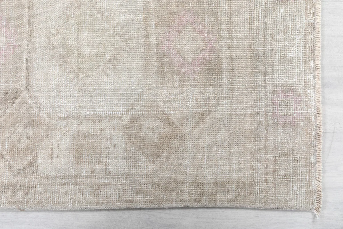 Close-up detail of the rug's faded beige and rose geometric pattern and edge