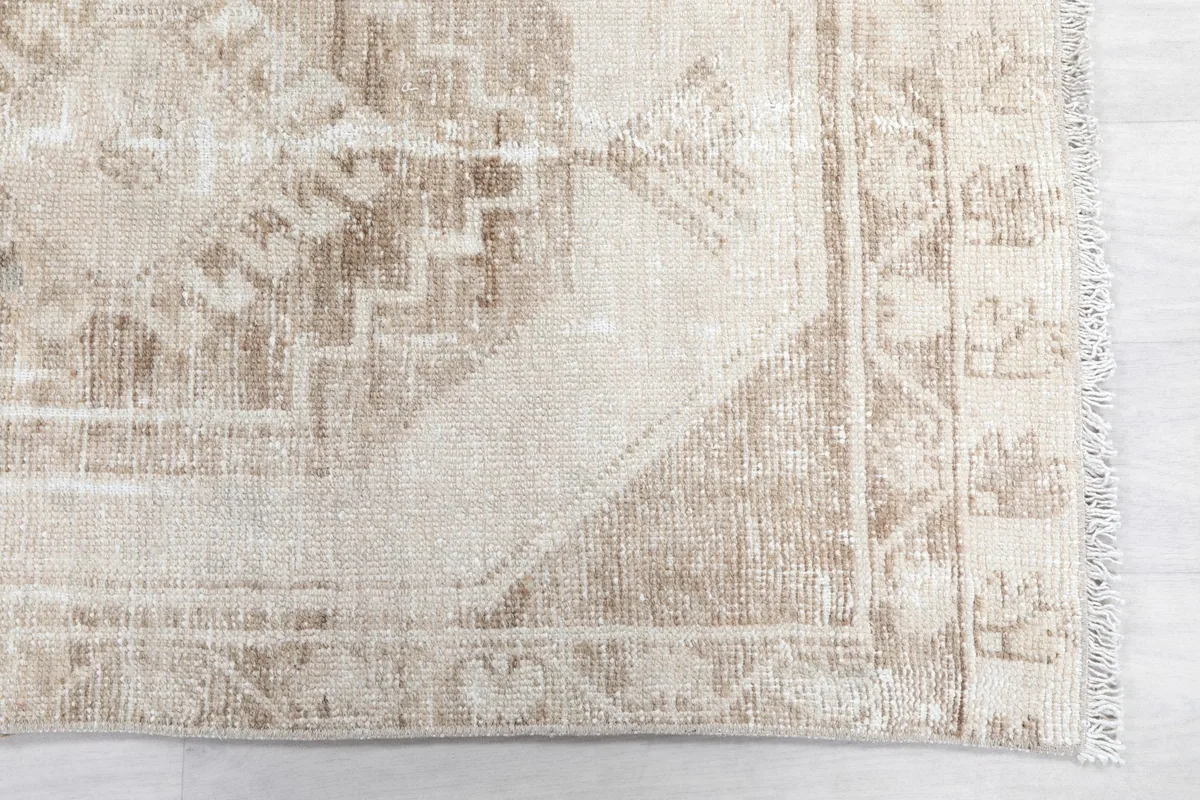 Detailed view of the rug's border and a corner, highlighting the faded beige and tan geometric patterns.