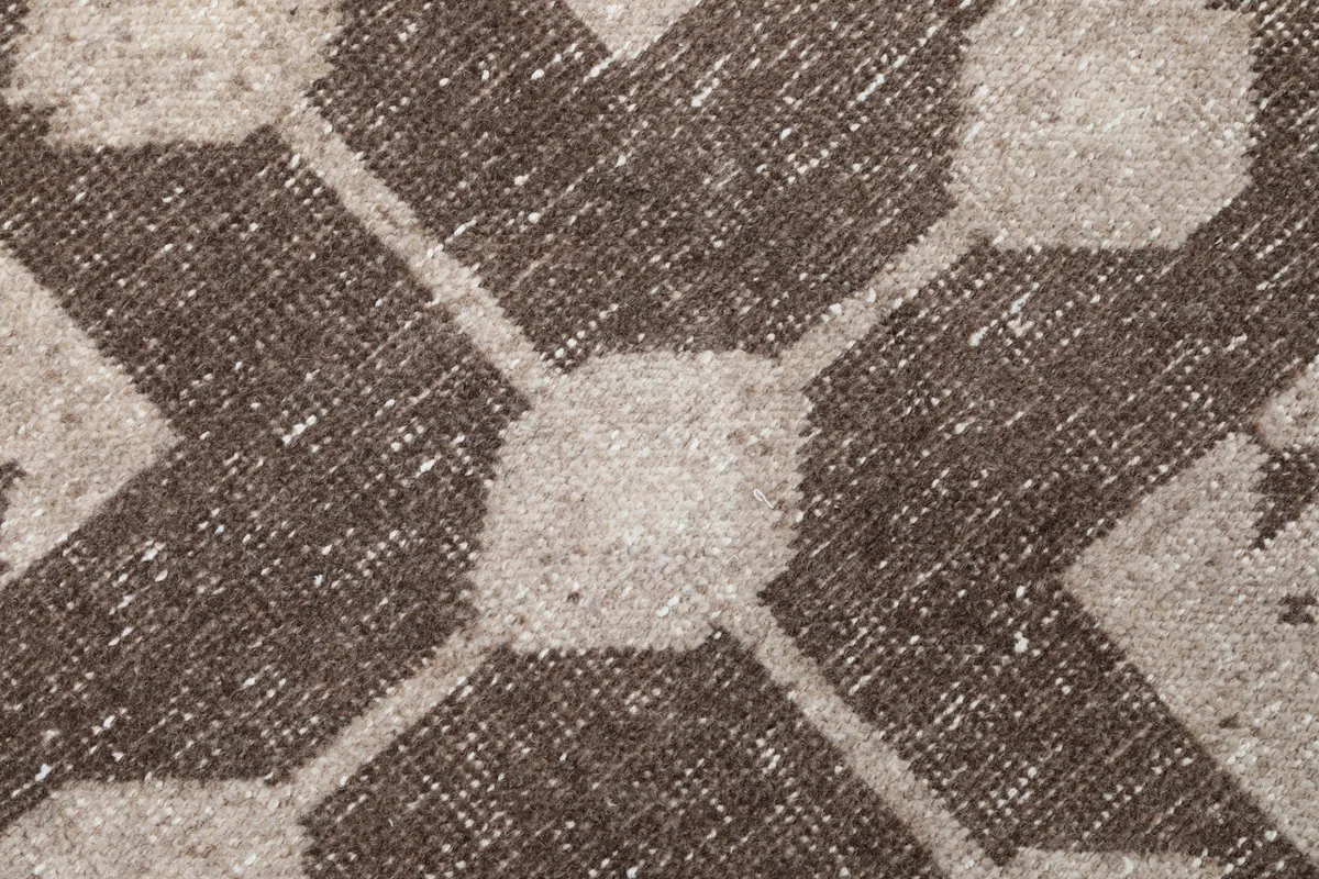Extreme close-up of the hand-knotted wool pile, revealing the texture and distressed brown geometric pattern.