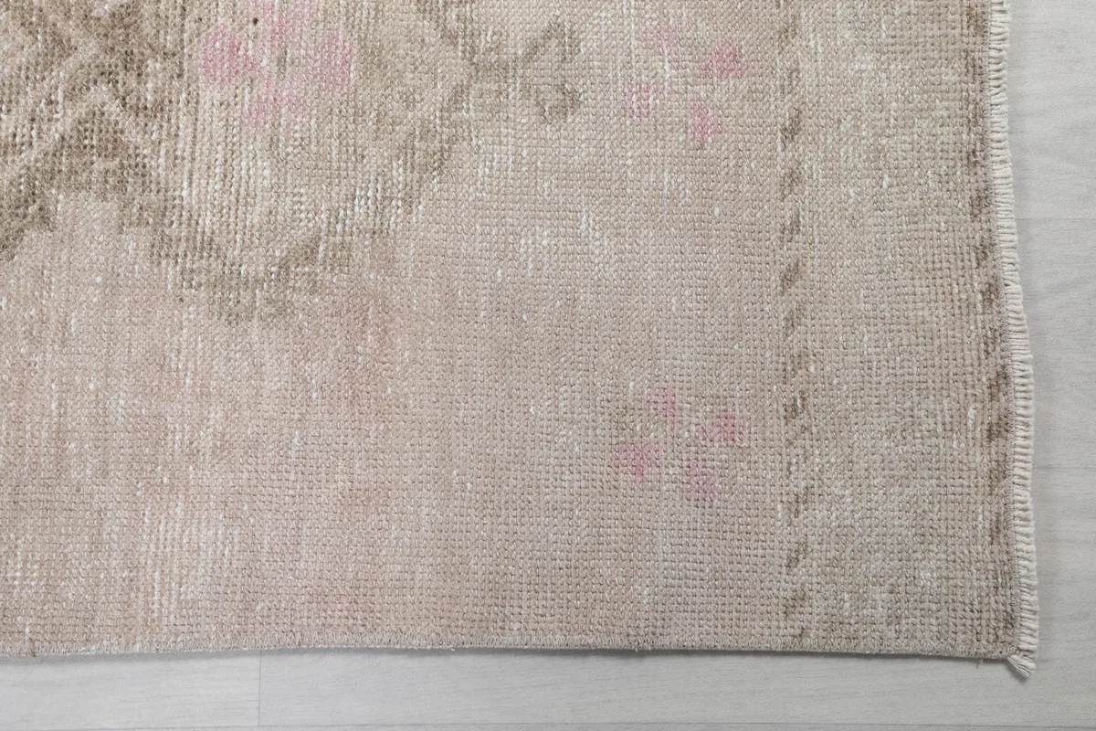 Detail view of the rug's edge and the soft beige and rose field with faint patterns