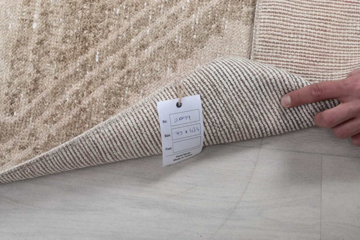Hand holding a corner of the rug, showing the back with a tag displaying size information