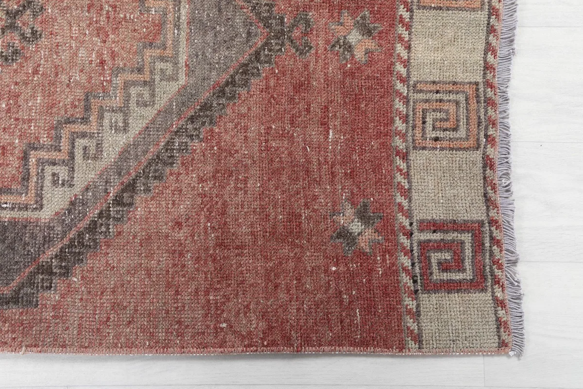 Detailed view of the rug's corner, showcasing the rust field, geometric border, and fringe.