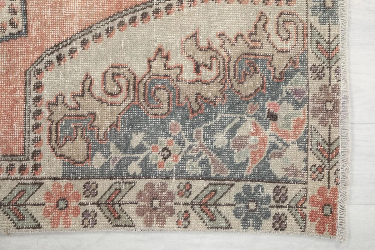 Detailed view of the corner motif with blue, gray, and rust floral patterns on the vintage rug.