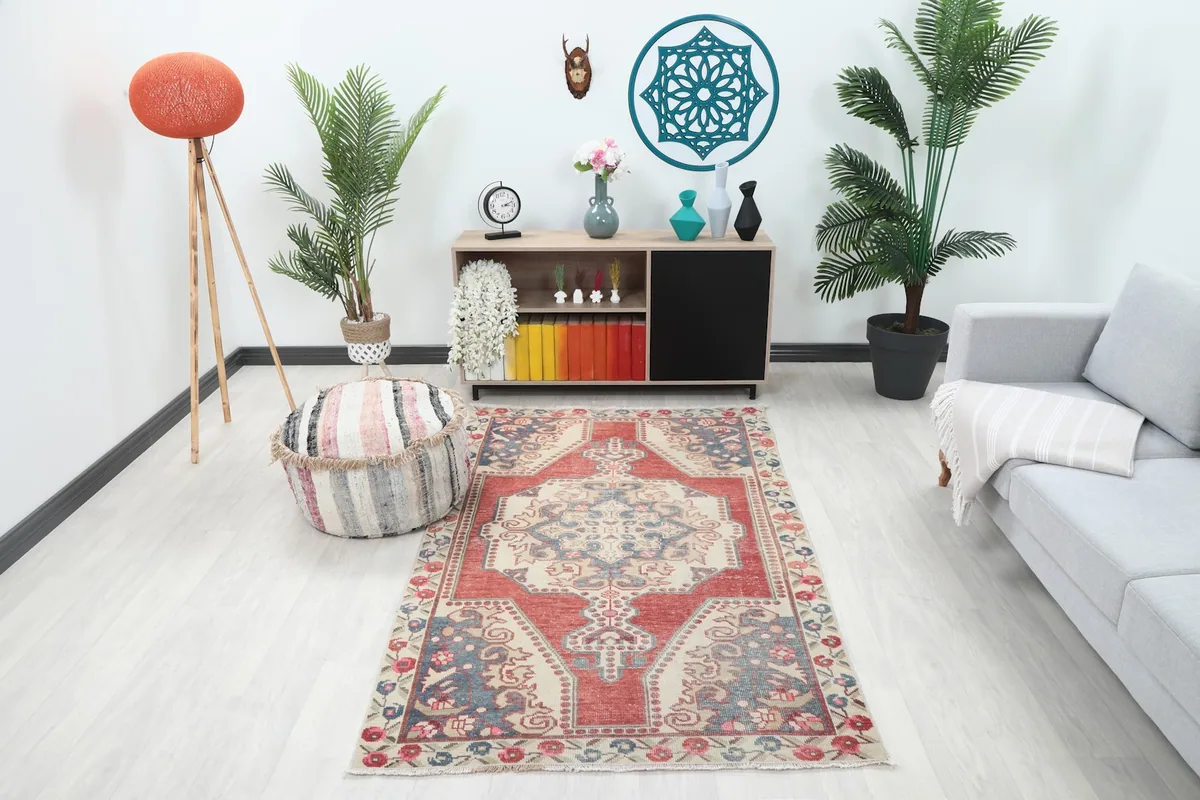Vintage red and ivory rug displayed in a living room setting with a sofa and plants