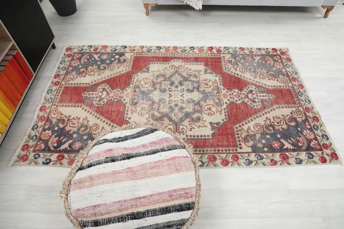 Full overhead view of the red and ivory rug with a striped pouf in the foreground