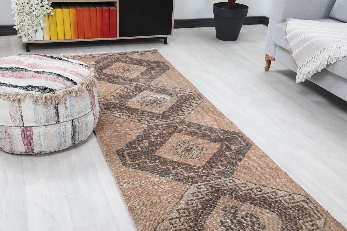 Close-up angle shot of the tan runner rug on the floor, showing the geometric patterns and a nearby ottoman.